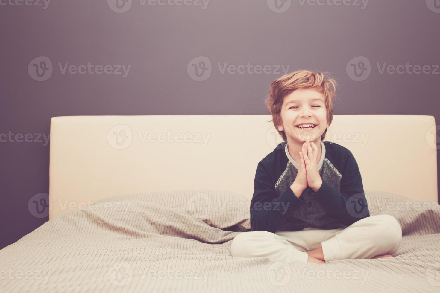 enfant heureux dans la pose de namaste pratiquant le yoga sur le lit. photo