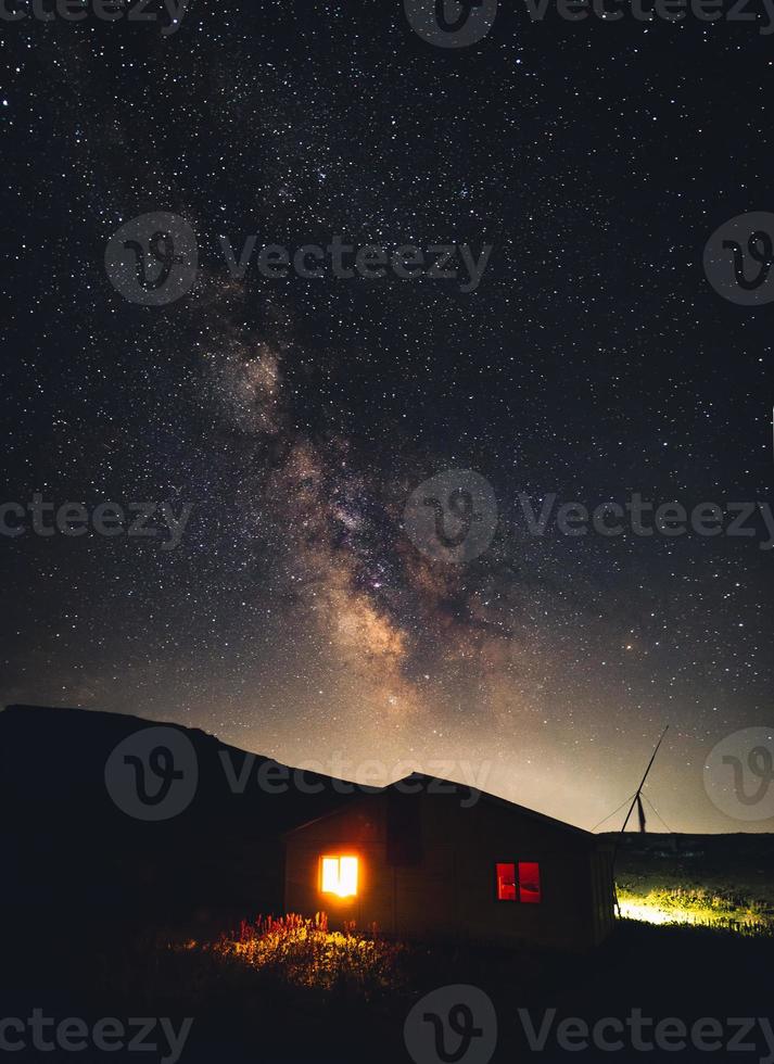 scène nocturne de la cabane en bois illuminée dans les montagnes isolées avec une scène nocturne étoilée de la voie lactée en été photo