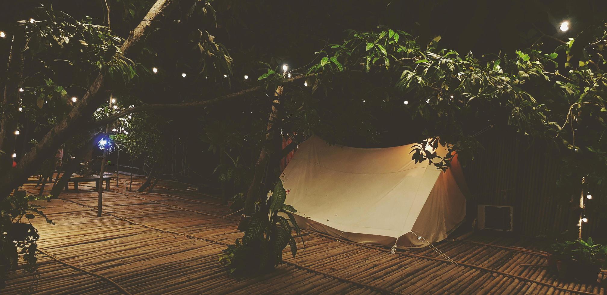 tente blanche sur sol en bambou sec avec arbre et éclairage décoré la nuit dans un ton vintage. concept de camping et d'activités photo