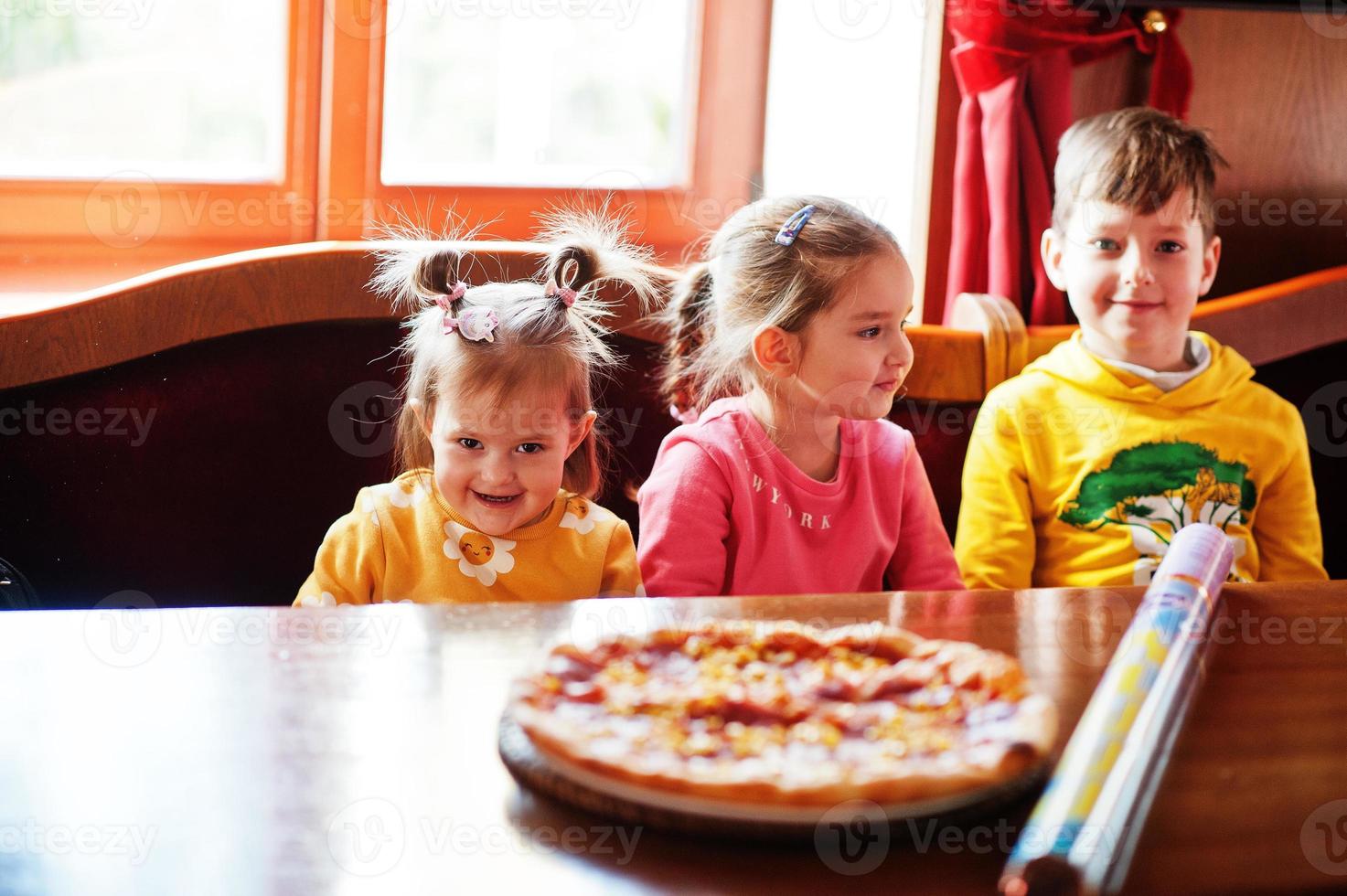 enfants le jour des anniversaires assis à table et mangeant de la pizza. photo