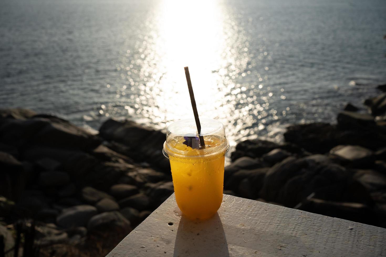 tasse de jus d'orange sur la table supérieure en bord de mer pendant la lumière du jour du ciel coucher de soleil. photo