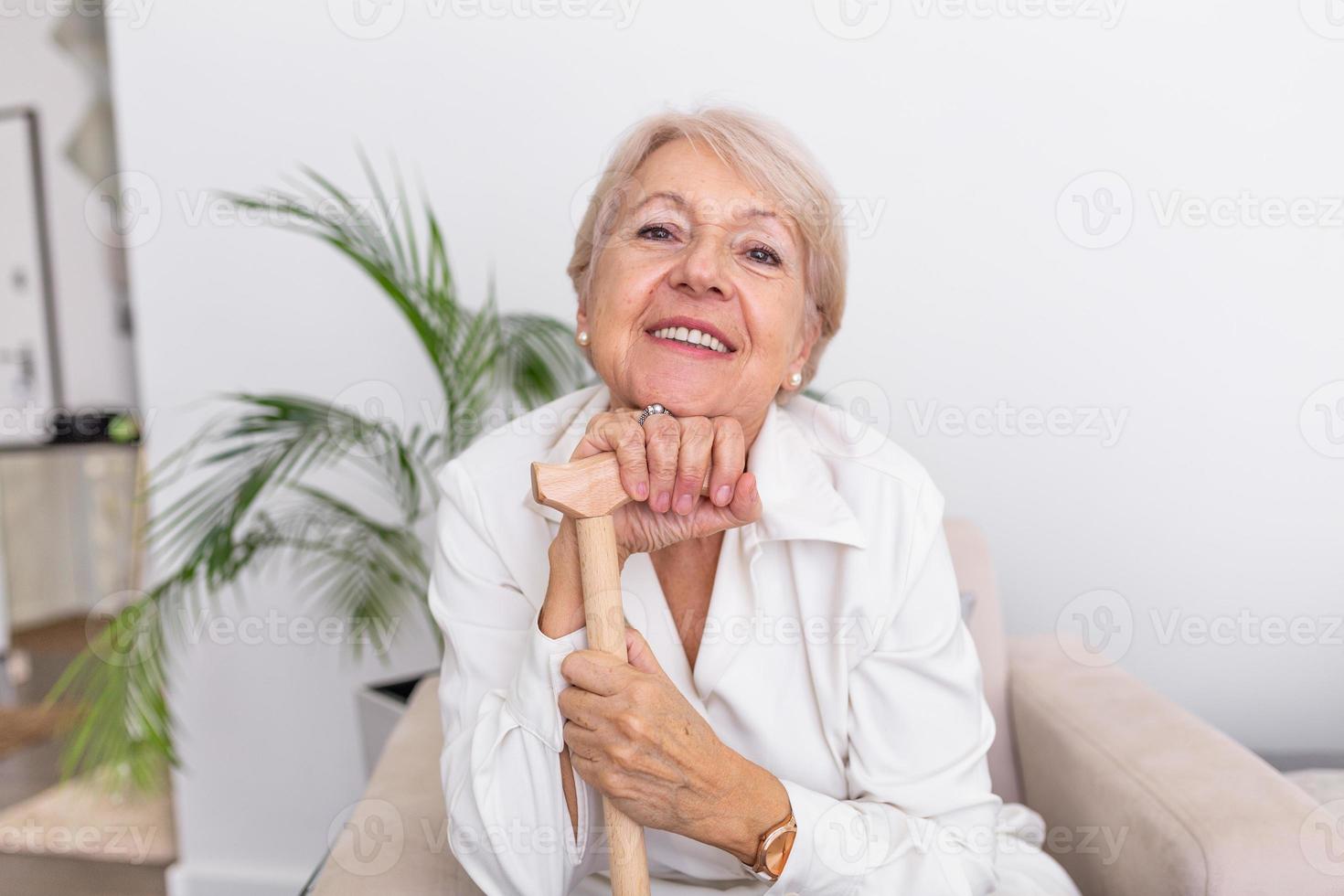 portrait d'une belle femme senior aux cheveux blancs et canne. portrait d'une femme âgée assise sur un canapé à la maison. femme d'âge mûr souriante aux cheveux gris mature regardant la caméra photo