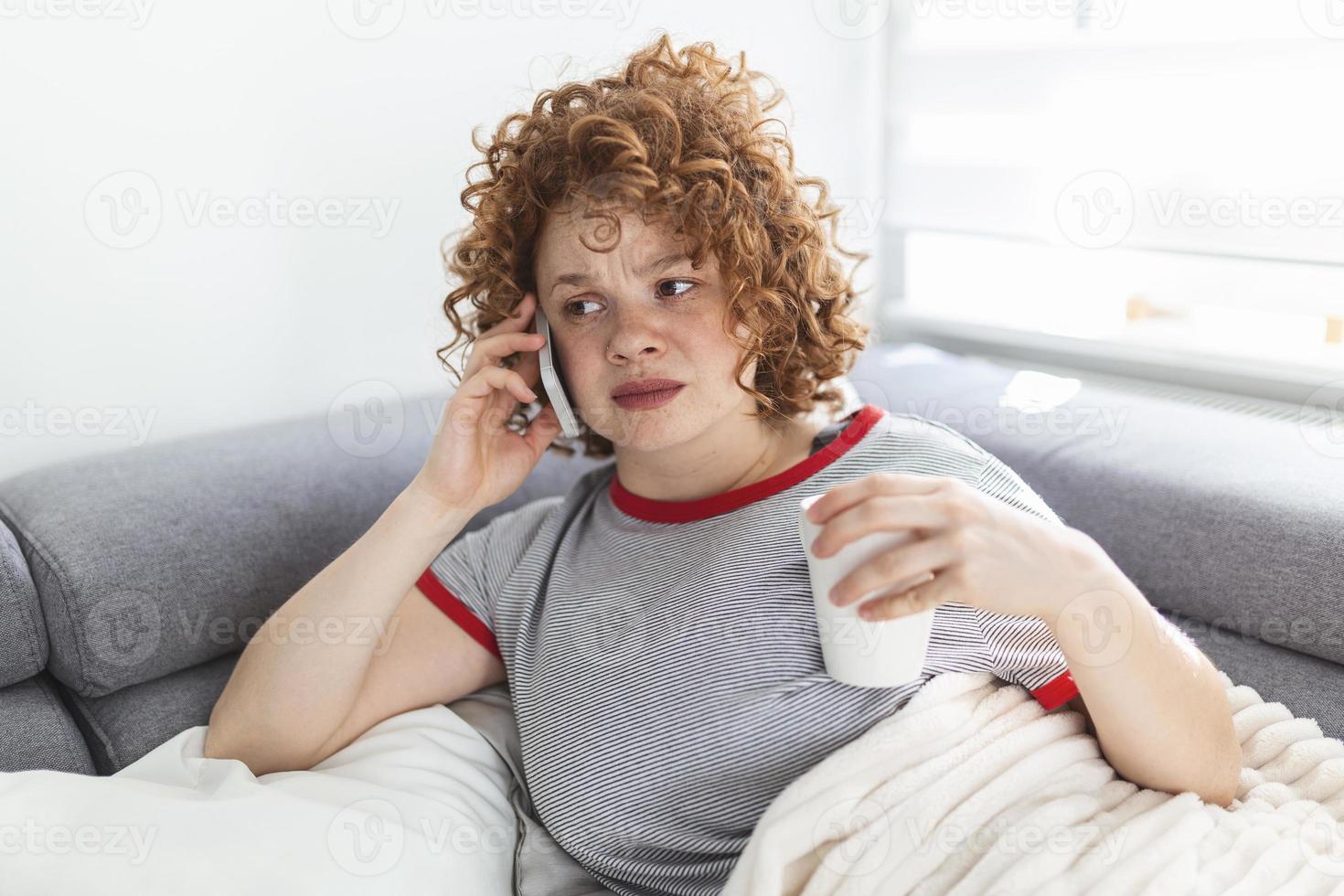 jeune femme recevant de mauvaises nouvelles par téléphone. femme malheureuse parlant au téléphone portable regardant vers le bas. une fille déprimée en pleurs tient un téléphone assis sur un canapé sans espoir, se sépare, a peur de menacer, d'abus mobiles photo