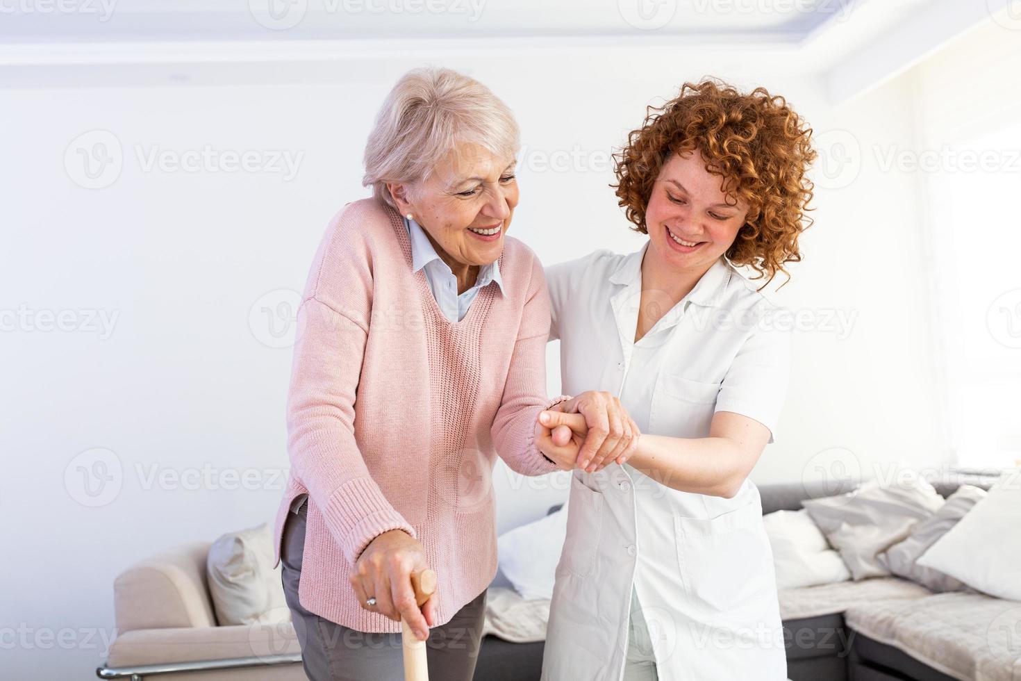 jeune soignant soutenant une femme handicapée âgée avec un bâton de marche. portrait d'une soignante heureuse et d'une femme âgée marchant ensemble à la maison. soignant professionnel prenant soin d'une femme âgée. photo