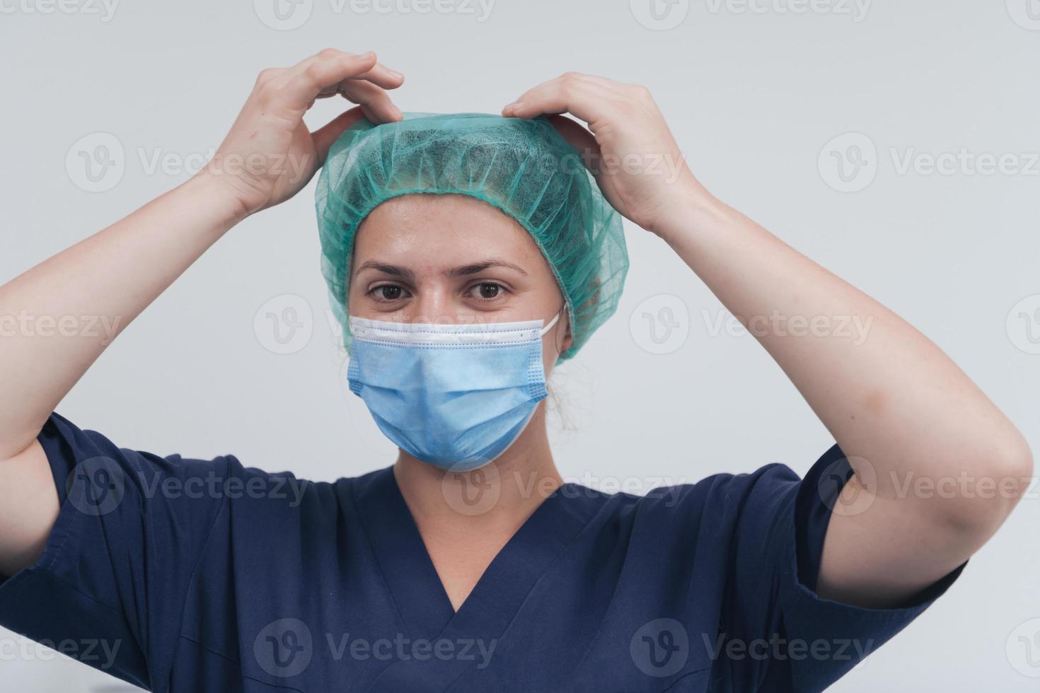 gros plan d'une femme médecin ou scientifique avec un masque médical et une casquette chirurgicale sur fond gris. elle ajuste le masque avec photo