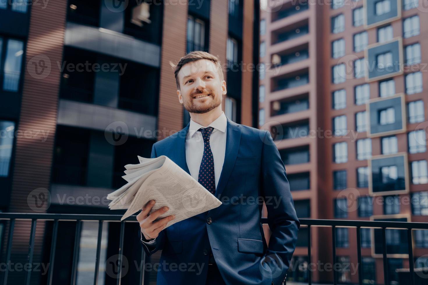 heureux PDG en costume bleu avec journal à côté des immeubles de bureaux photo