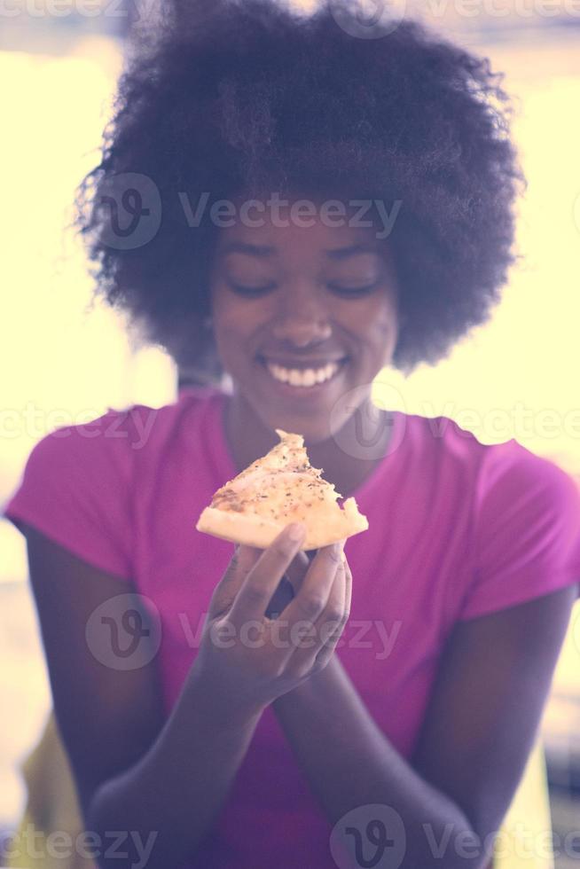 femme avec une coiffure afro mangeant une tranche de pizza savoureuse photo