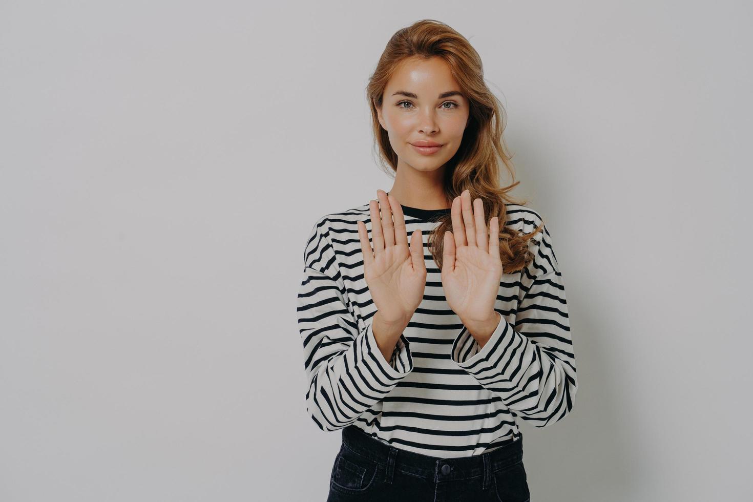 jeune femme confiante gesticulant panneau d'arrêt, disant non tout en se tenant isolé contre le mur gris photo