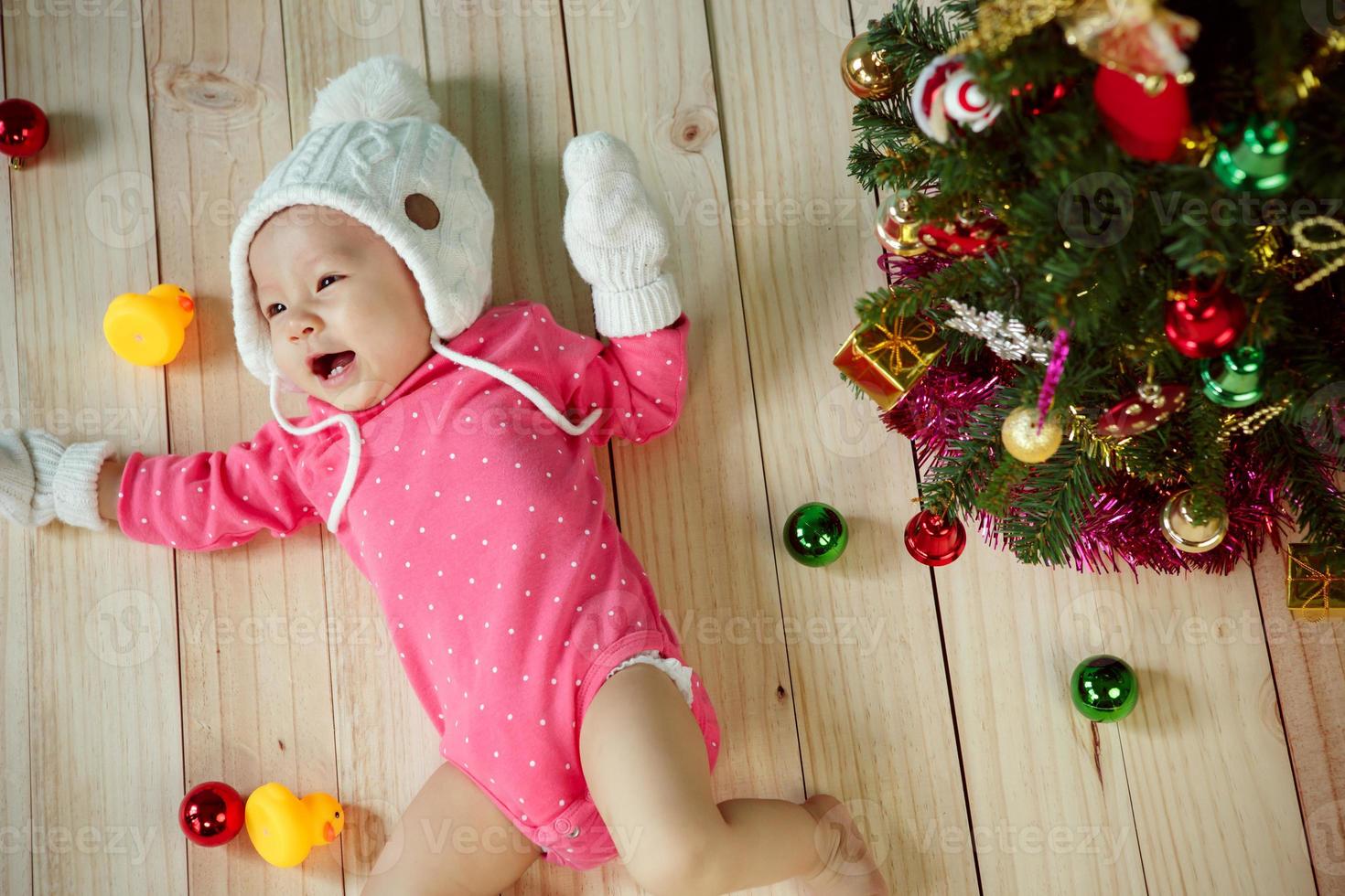 enfant en bas âge avec chapeau de caniche blanc et mitaines tricotées et décoration d'arbre de noël sur fond vert photo