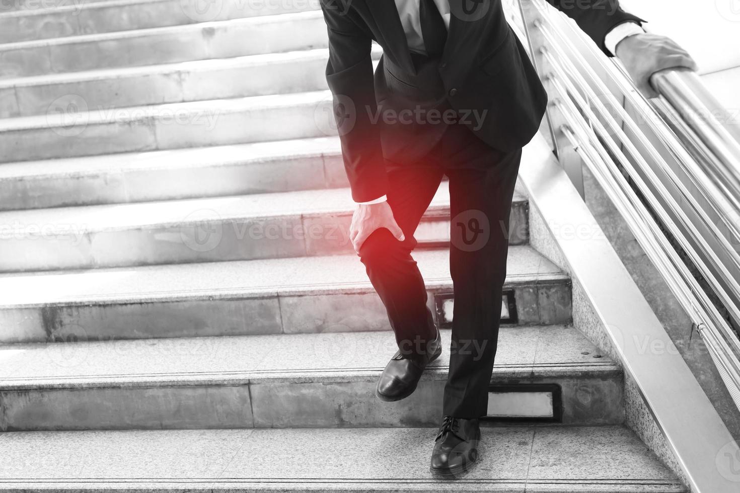 un homme d'affaires en costume a la douleur douloureuse et l'expression douloureuse du problème du genou et monte et descend dans l'escalier pendant qu'il va au bureau. notion de soins de santé. photo