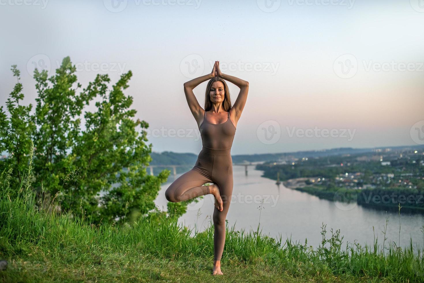 une jeune gymnaste fait du yoga dans la nature dans un parc contre le ciel, en utilisant une combinaison de poses de yoga traditionnelles, de pilates et de danse douce. lien avec la nature. photo