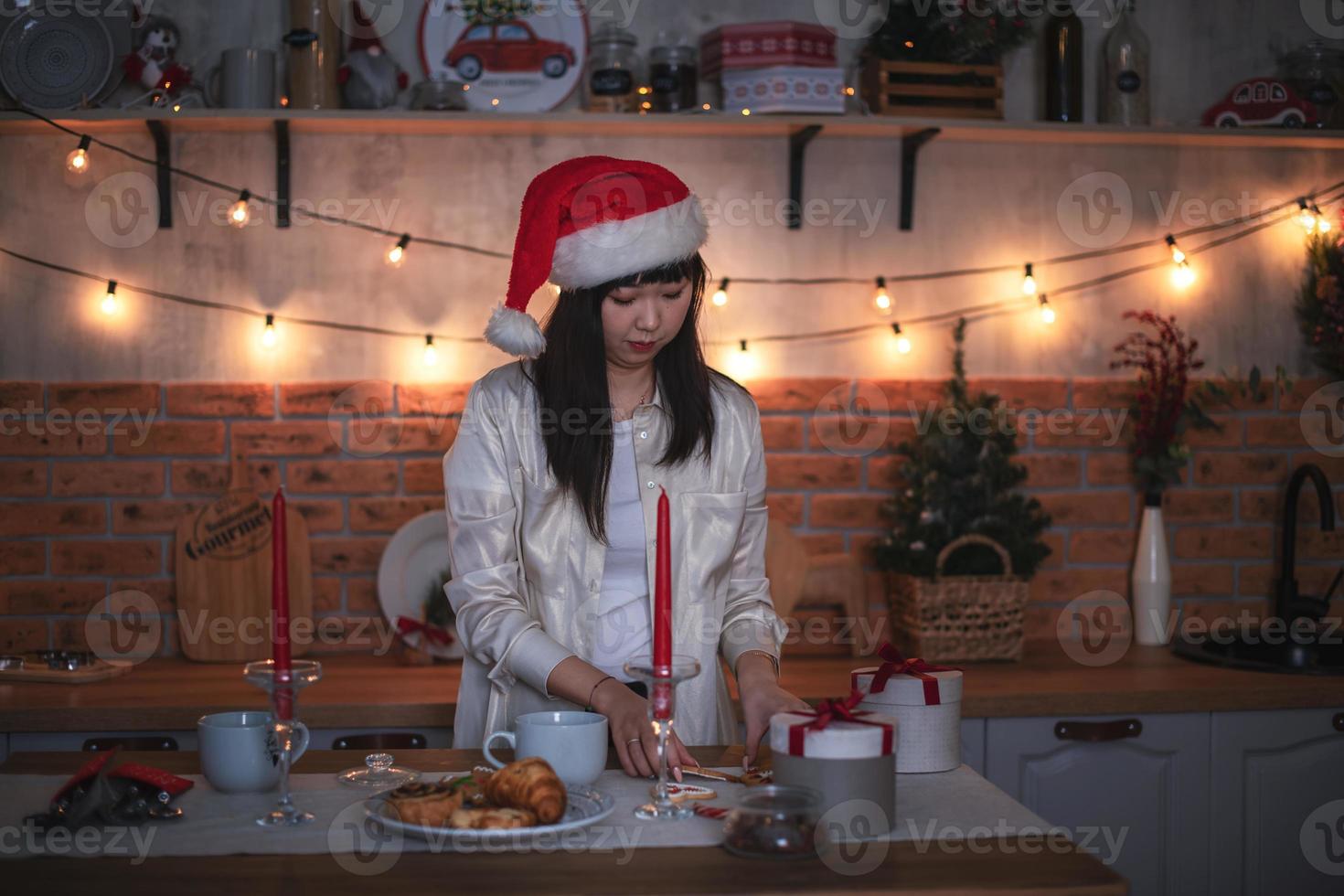 une jeune femme coréenne dans un chapeau de père noël cuisine le soir dans une cuisine décorée pour noël. photo