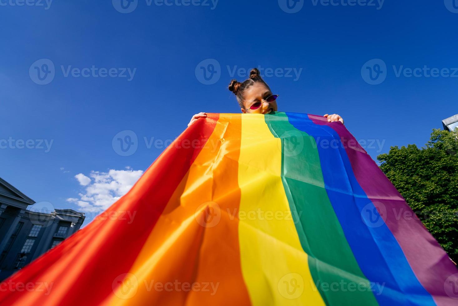 une jeune femme développe un drapeau arc-en-ciel contre le ciel photo