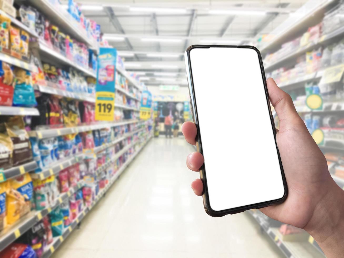 concept de shopping intelligent téléphone portable à la main devant les étagères de marchandises dans les supermarchés et les épiceries. maquette d'écran blanc vierge pour votre propre créativité. photo