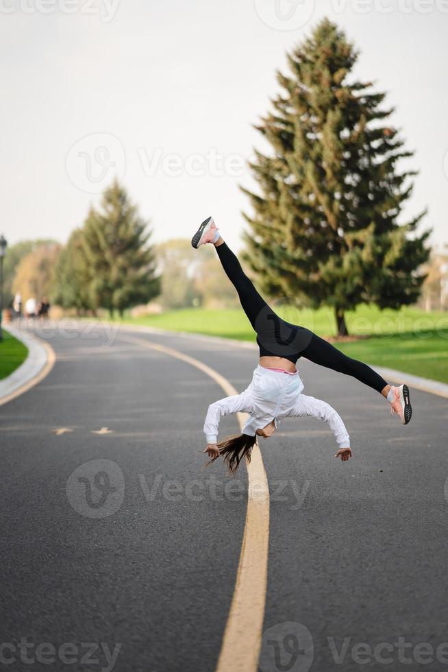 femme athlète sautant culbute sur la route, faisant des exercices à l'extérieur. photo