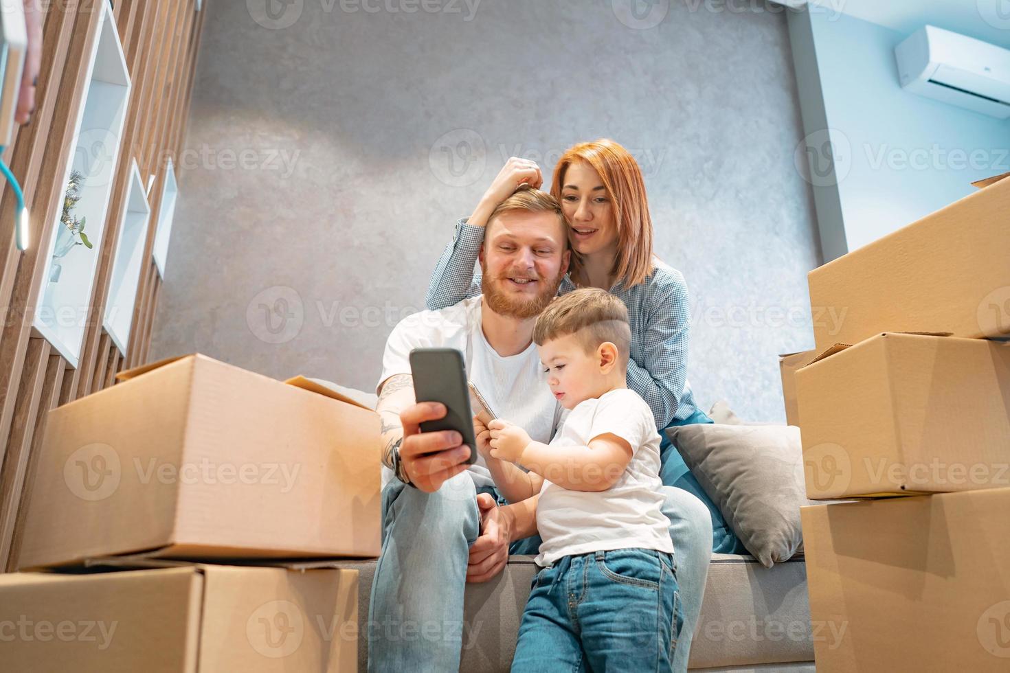 jeune famille heureuse avec enfant déballant des boîtes ensemble assis sur un canapé photo