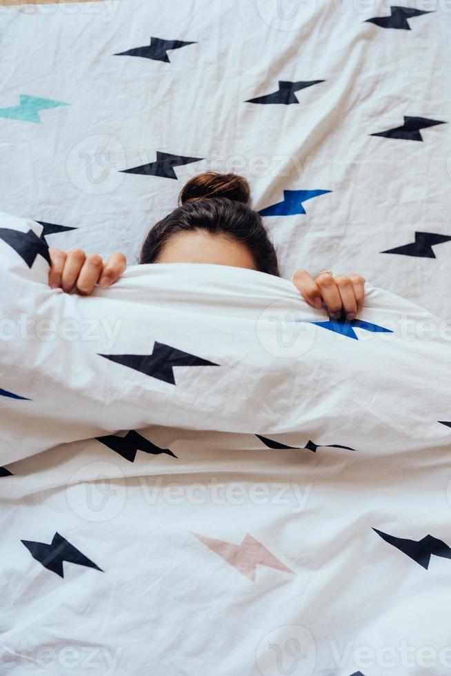 gros plan d'une belle jeune femme se trouve dans son lit recouvert d'une couverture. photo