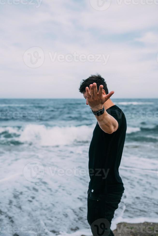 un gars souriant dans un t-shirt noir se dresse sur le bord de mer sablonneux. photo