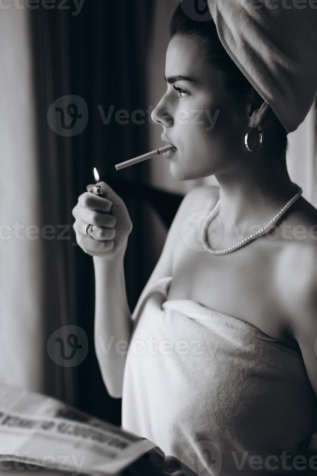 belle jeune femme dans une serviette fume une cigarette et lit le journal photo