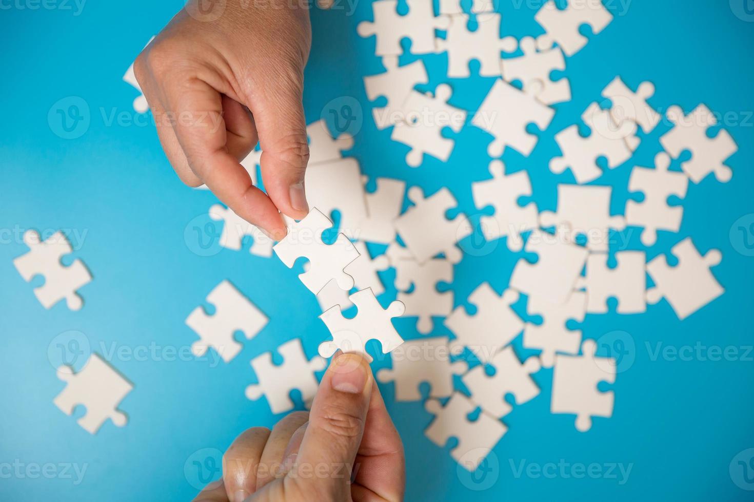 gros plan main tenant et jouant au jeu de puzzle incomplet. partie blanche des pièces de puzzle sur fond bleu. concepts de résolution de problèmes, d'affaires, de travail d'équipe. photo