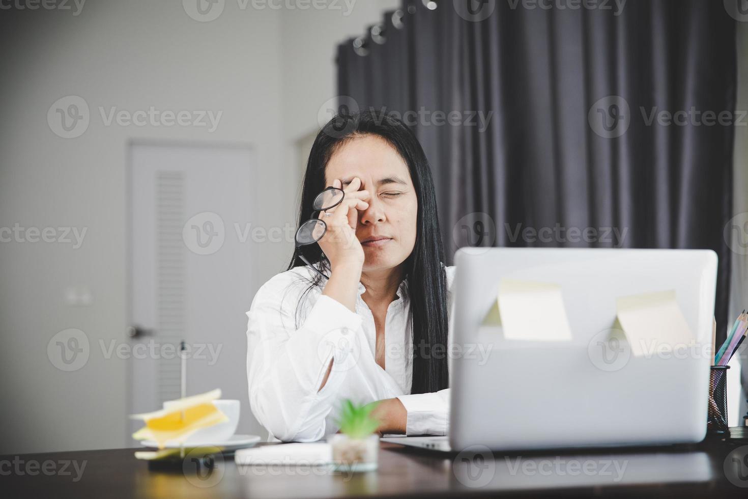 jeune femme d'affaires somnolente et a des problèmes oculaires frustrants avec la maladie de céphalée due à l'utilisation d'un ordinateur portable sur son bureau. employée stressée fatiguée et épuisée par le surmenage. photo