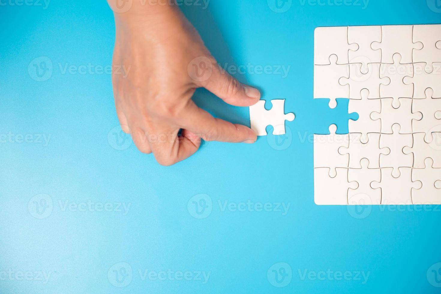 gros plan main tenant et jouant au jeu de puzzle incomplet. partie blanche des pièces de puzzle sur fond bleu. concepts de résolution de problèmes, d'affaires, de travail d'équipe. photo