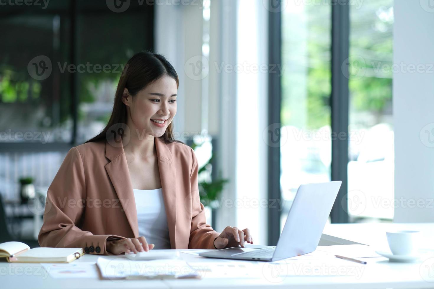 belle femme d'affaires asiatique analyse les graphiques à l'aide d'une calculatrice d'ordinateur portable au bureau. photo