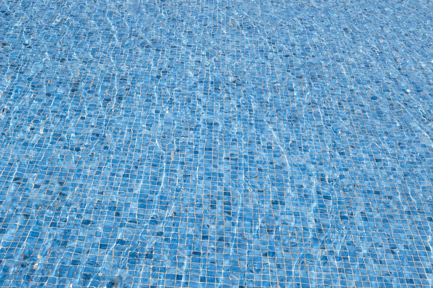 le vent fait onduler l'eau. arrière-plan abstrait de l'eau de surface claire. piscine bleue reflétant le soleil ridée. motif du fond de la piscine en carreaux bleus en céramique mosaïque ondulée. photo