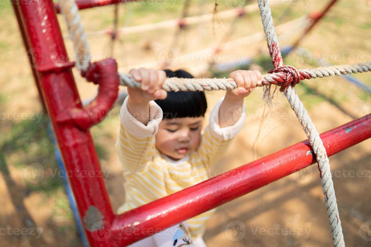 jolie fille asiatique sourire jouer sur la cour ou l'aire de jeux de l'école ou de la maternelle. activité estivale saine pour les enfants. petite fille asiatique grimpant à l'extérieur sur l'aire de jeux. enfant jouant sur une aire de jeux extérieure. photo