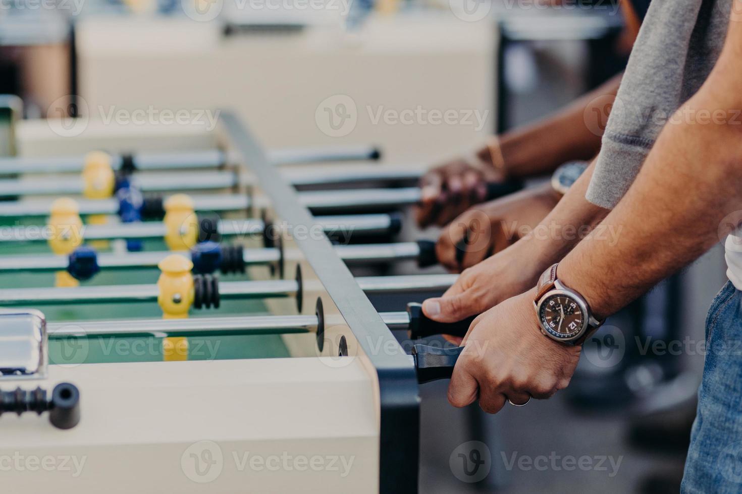 des hommes méconnaissables jouent au baby-foot, apprécient le jeu d'équipe, veulent gagner des adversaires, passent du temps libre au pub. jeu de kick. match de foot sur table photo