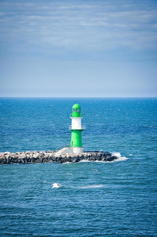 phare blanc vert sur la rivière warnow à rostock. vagues sur le bord de la pierre photo