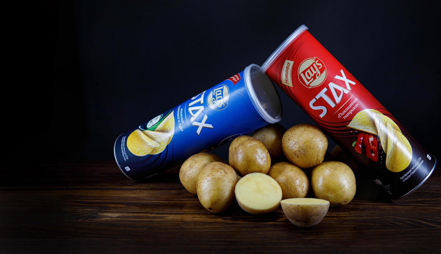 krasnoyarsk, russie - 05 janvier 2022 deux boîtes de chips se trouvent sur une table à côté de pommes de terre fraîches sur fond sombre. photo