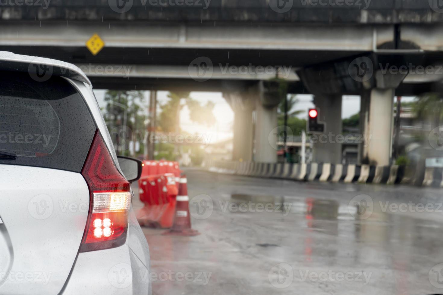 face arrière de la voiture blanche avec clignotant mouillé de pluie. surface de route en béton mouillée de pluie. garé à un feu rouge sous un pont nivelé. gouttelettes d'eau floues de la surface de la route. photo