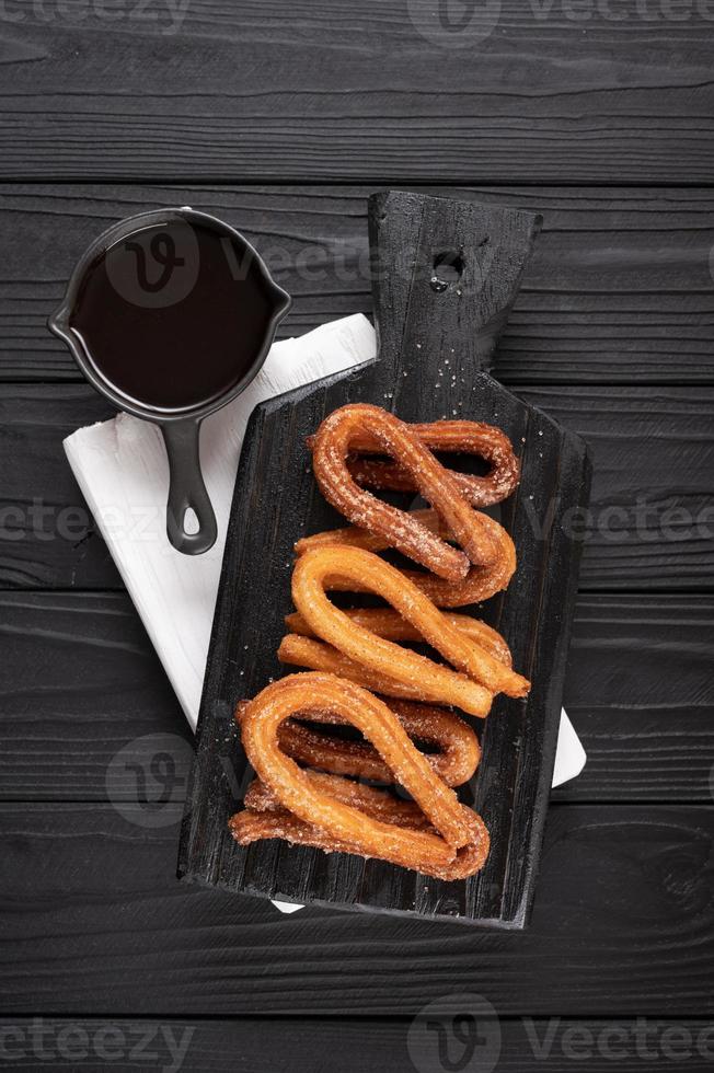 churros faits maison avec du chocolat sur un fond rustique en bois foncé. photo