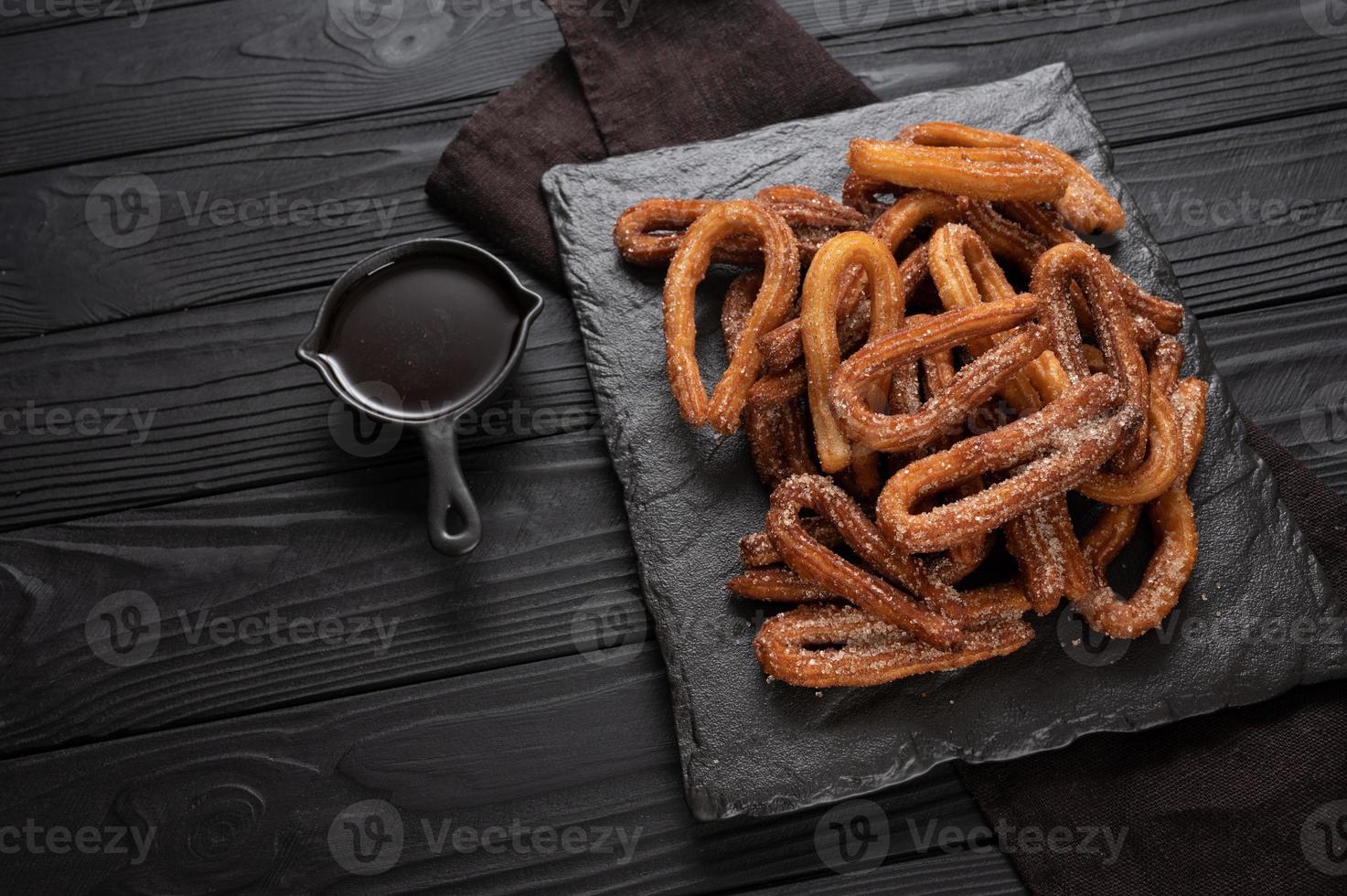 churros faits maison avec du chocolat sur un fond rustique en bois foncé. photo