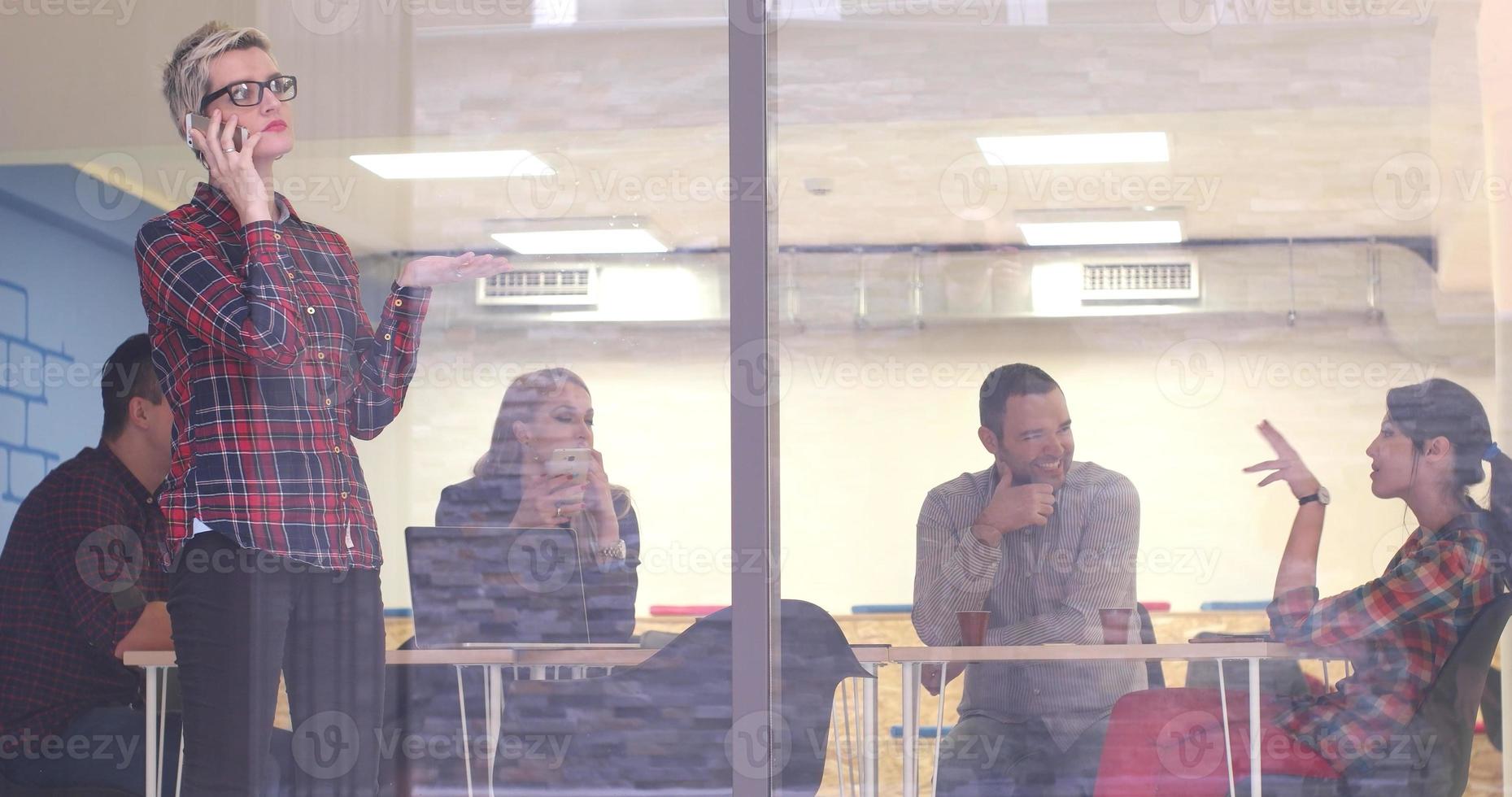 femme d'affaires regardant à travers une fenêtre et utilisant un téléphone portable lors d'une réunion d'affaires photo