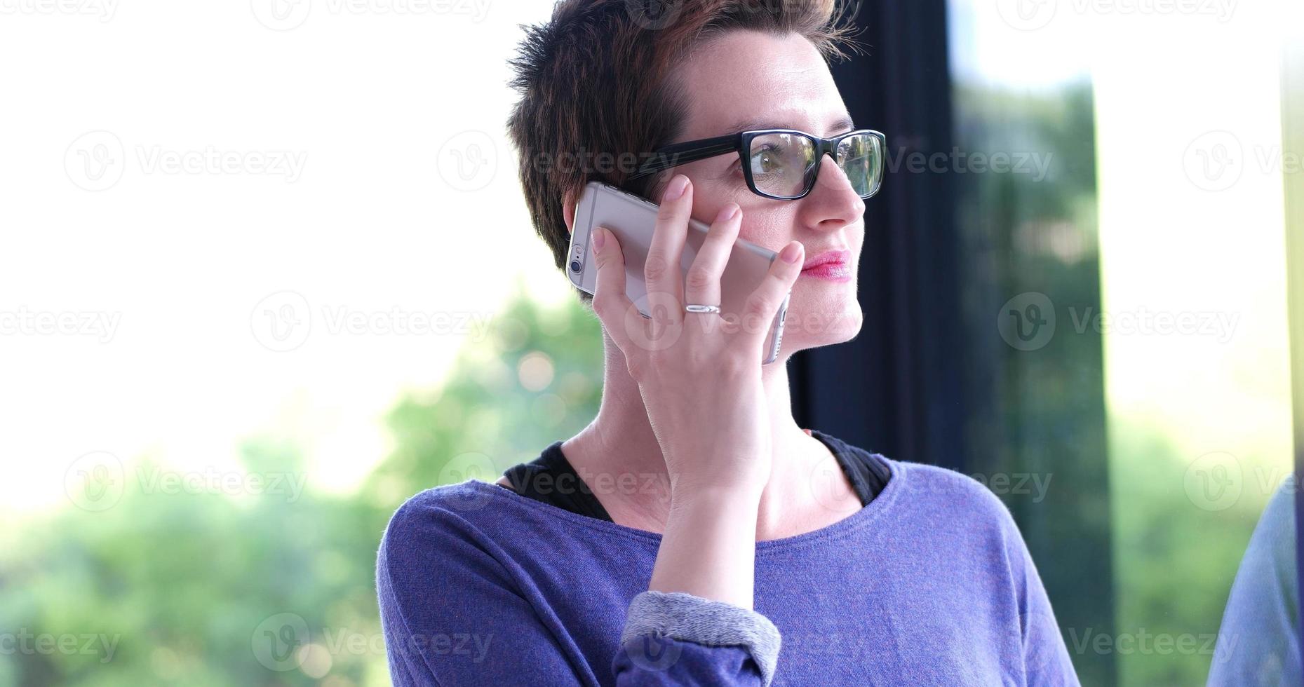 femme élégante utilisant un téléphone portable par fenêtre dans un immeuble de bureaux photo