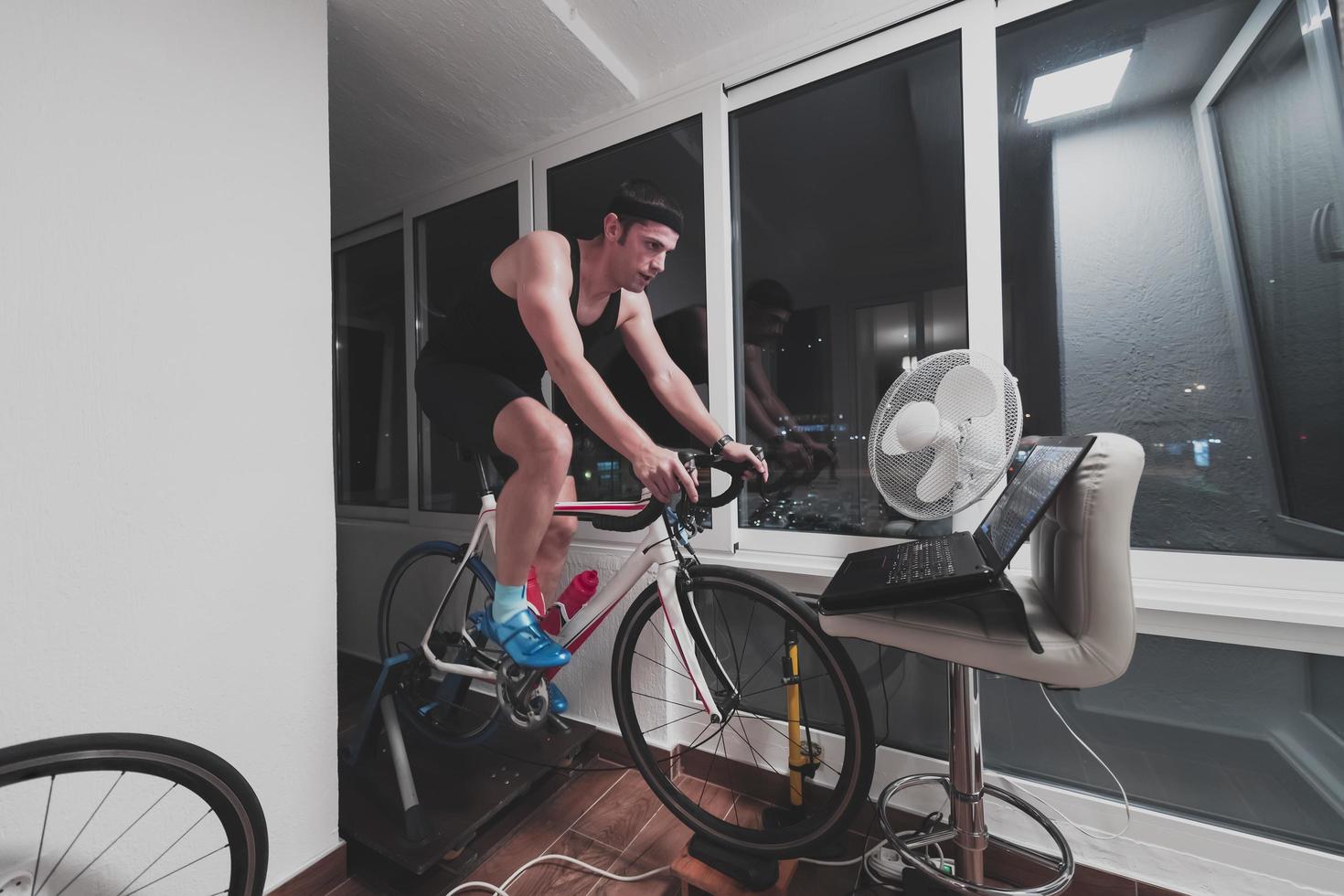 homme faisant du vélo sur l'entraîneur de la machine il s'exerce à la maison la nuit en jouant au jeu de course de vélo en ligne photo