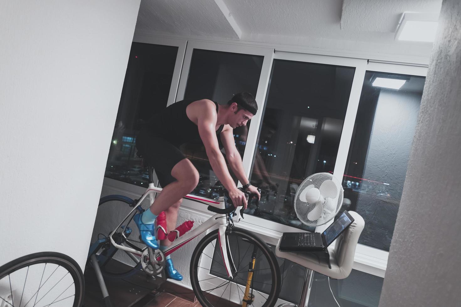 homme faisant du vélo sur l'entraîneur de la machine il s'exerce à la maison la nuit en jouant au jeu de course de vélo en ligne photo