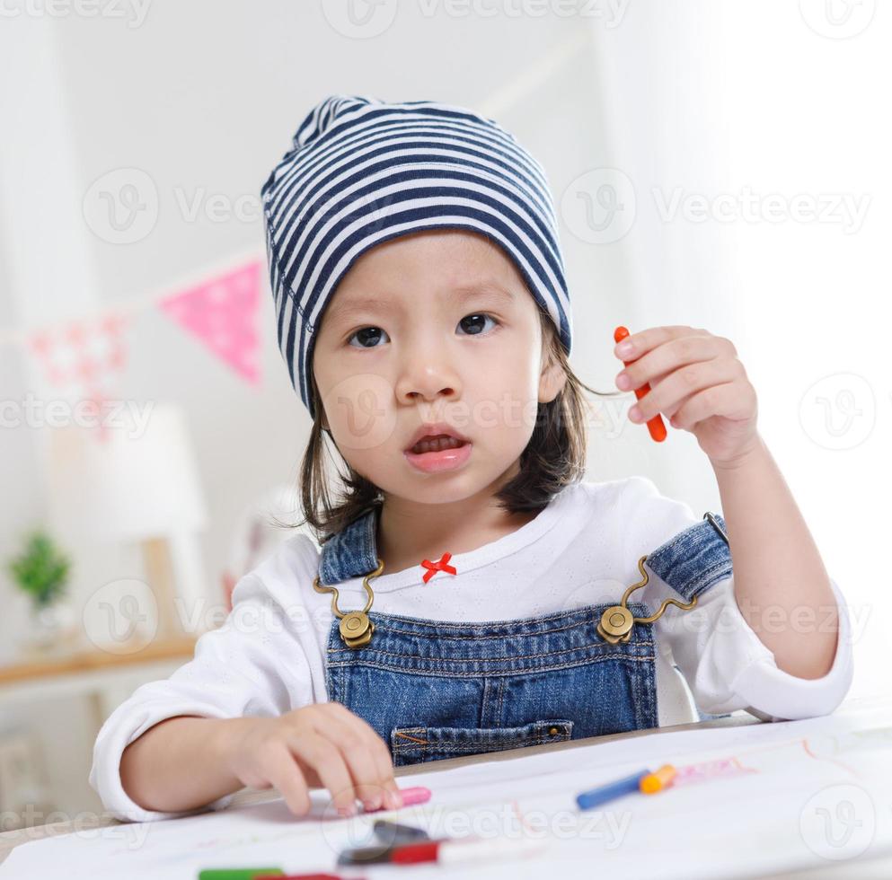 petite fille asiatique assise à table dans la chambre, fille d'âge préscolaire dessinant sur papier avec des stylos colorés le jour ensoleillé, jardin d'enfants ou photo