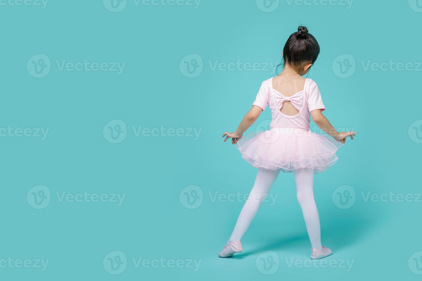 belle petite fille asiatique souriante dans un costume rose danse un ballet à l'école, espace vide en studio tourné isolé sur fond bleu coloré photo