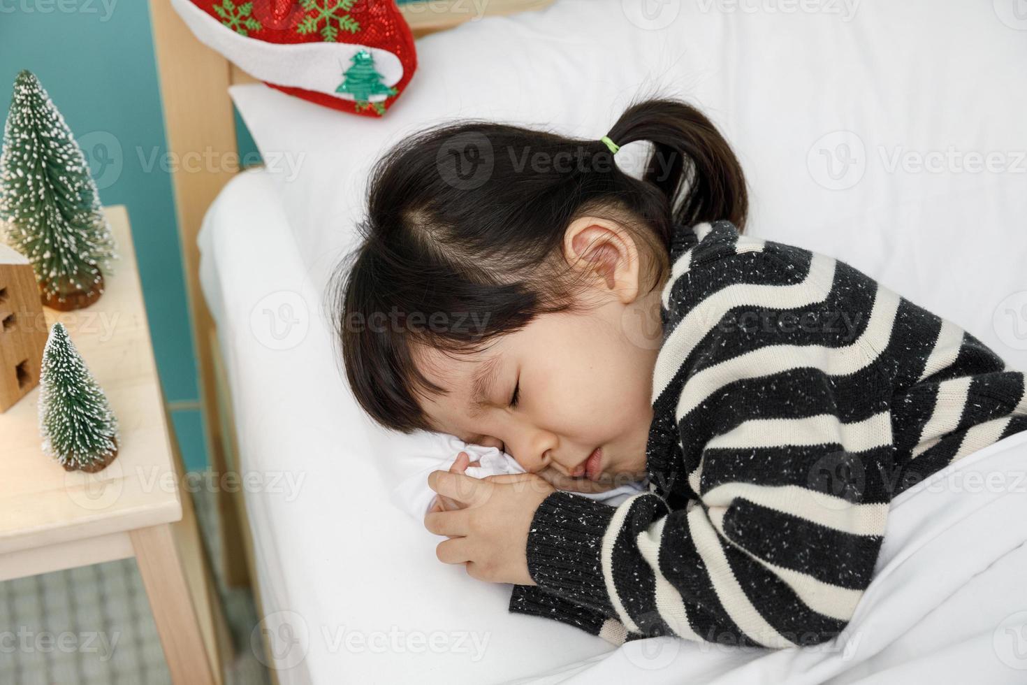 enfant fille dormant sur le lit en bois dans sa chambre, heureuse petite fille asiatique dormir avec une couverture sur le lit, concept de noël photo