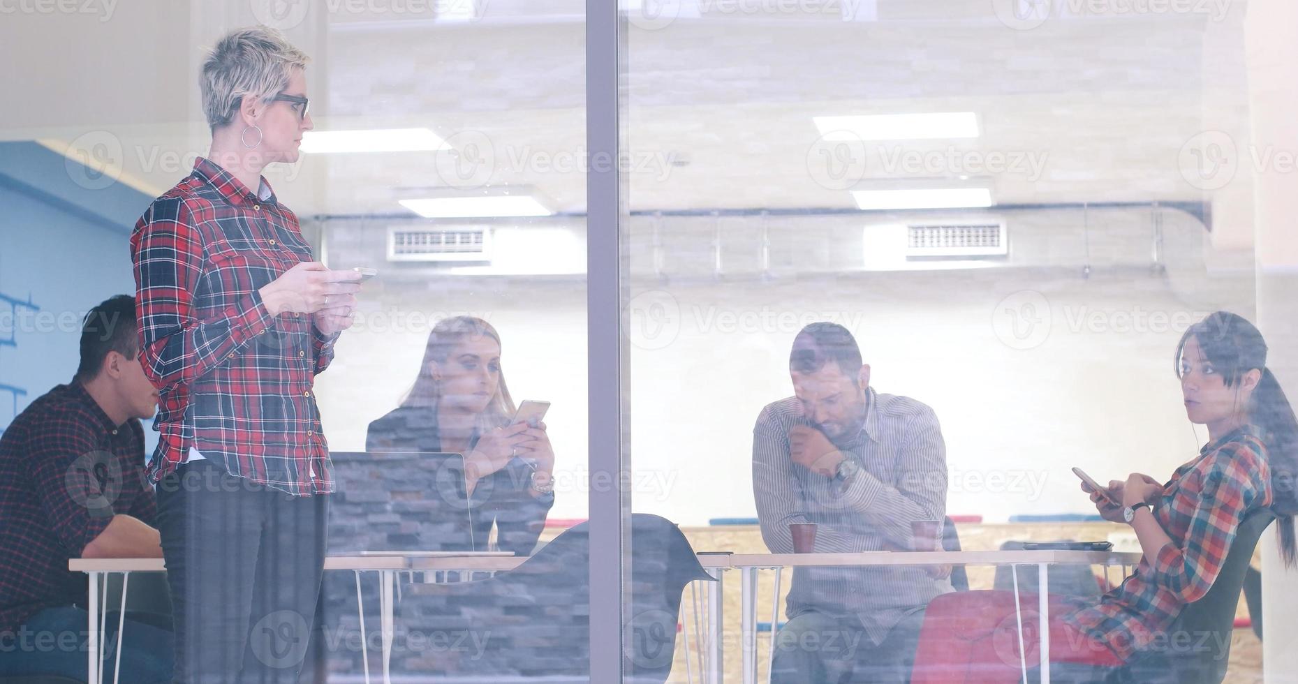 femme d'affaires regardant à travers une fenêtre et utilisant un téléphone portable lors d'une réunion d'affaires photo