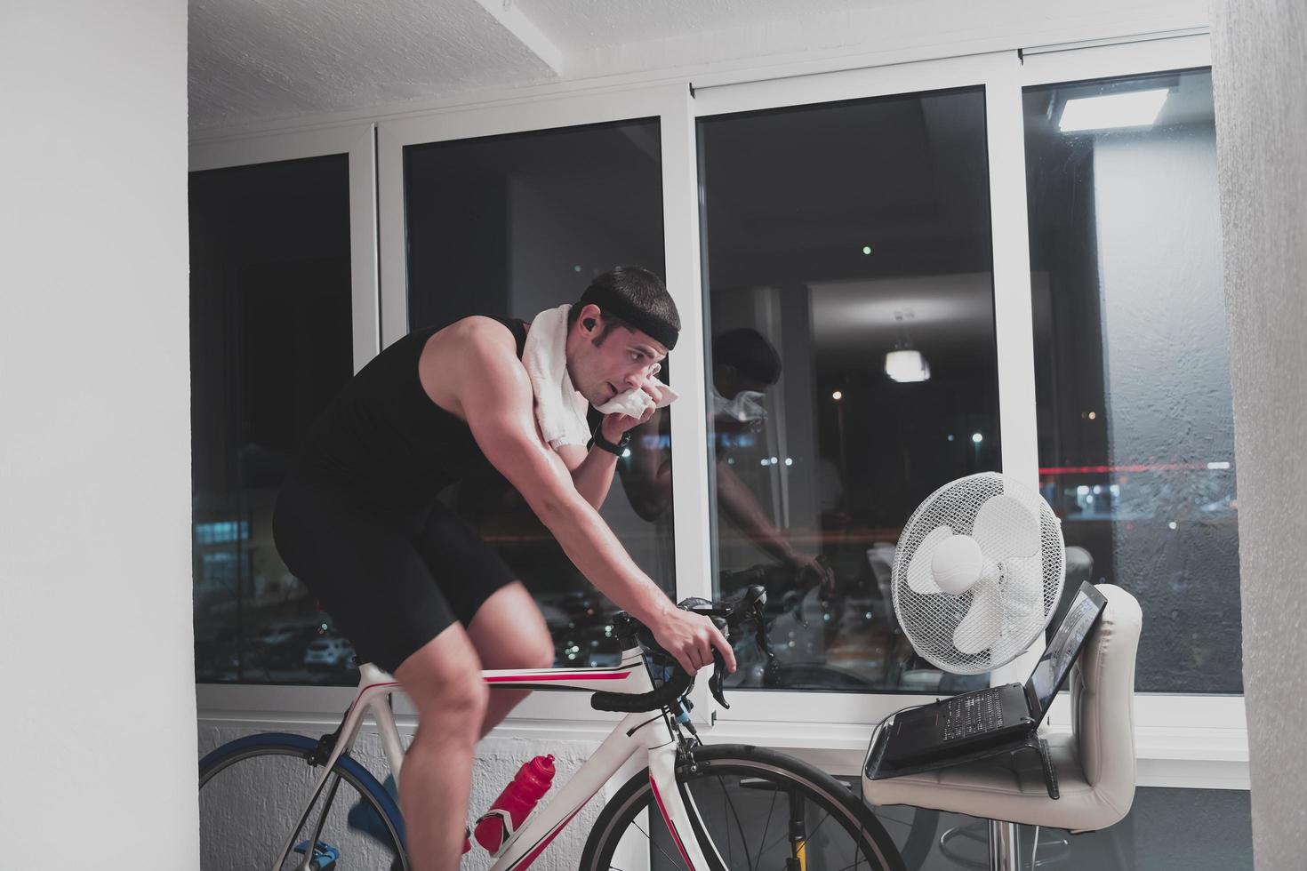 homme faisant du vélo sur l'entraîneur de la machine il s'exerce à la maison la nuit en jouant au jeu de course de vélo en ligne photo