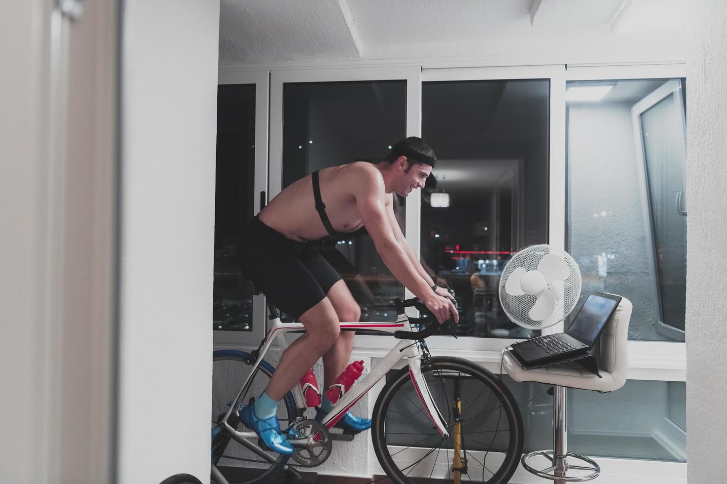 homme faisant du vélo sur l'entraîneur de la machine il s'exerce à la maison la nuit en jouant au jeu de course de vélo en ligne photo