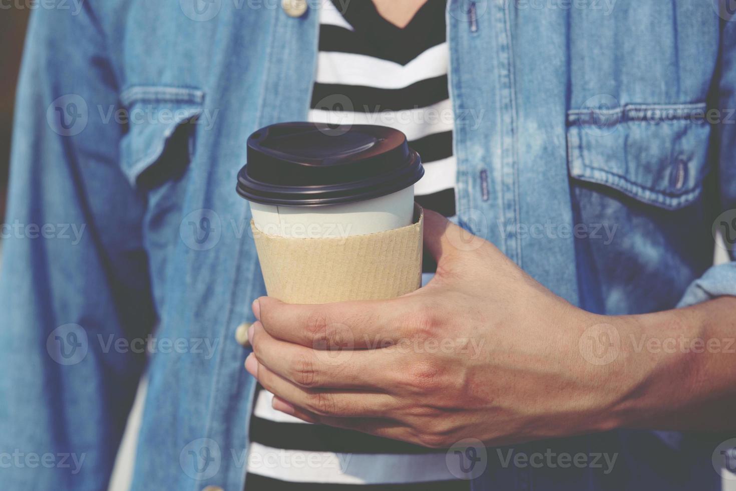 jeune homme main tenant une tasse de papier à emporter en buvant du café chaud sur le café-café. photo