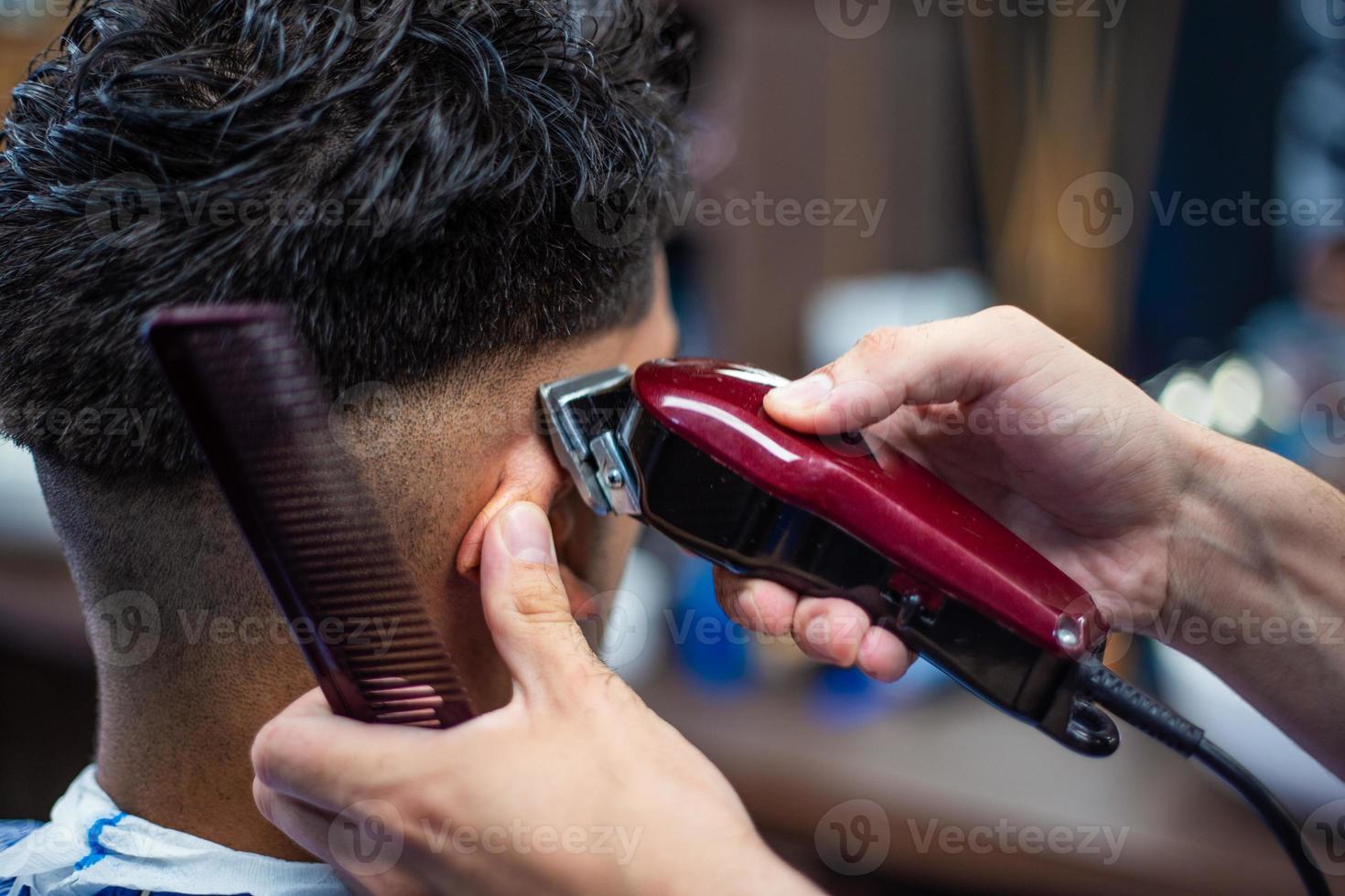 gros plan d'un homme qui se fait couper les cheveux à la mode au salon de  coiffure. coiffeur masculin servant le client, faisant une coupe de cheveux  à l'aide d'une machine et