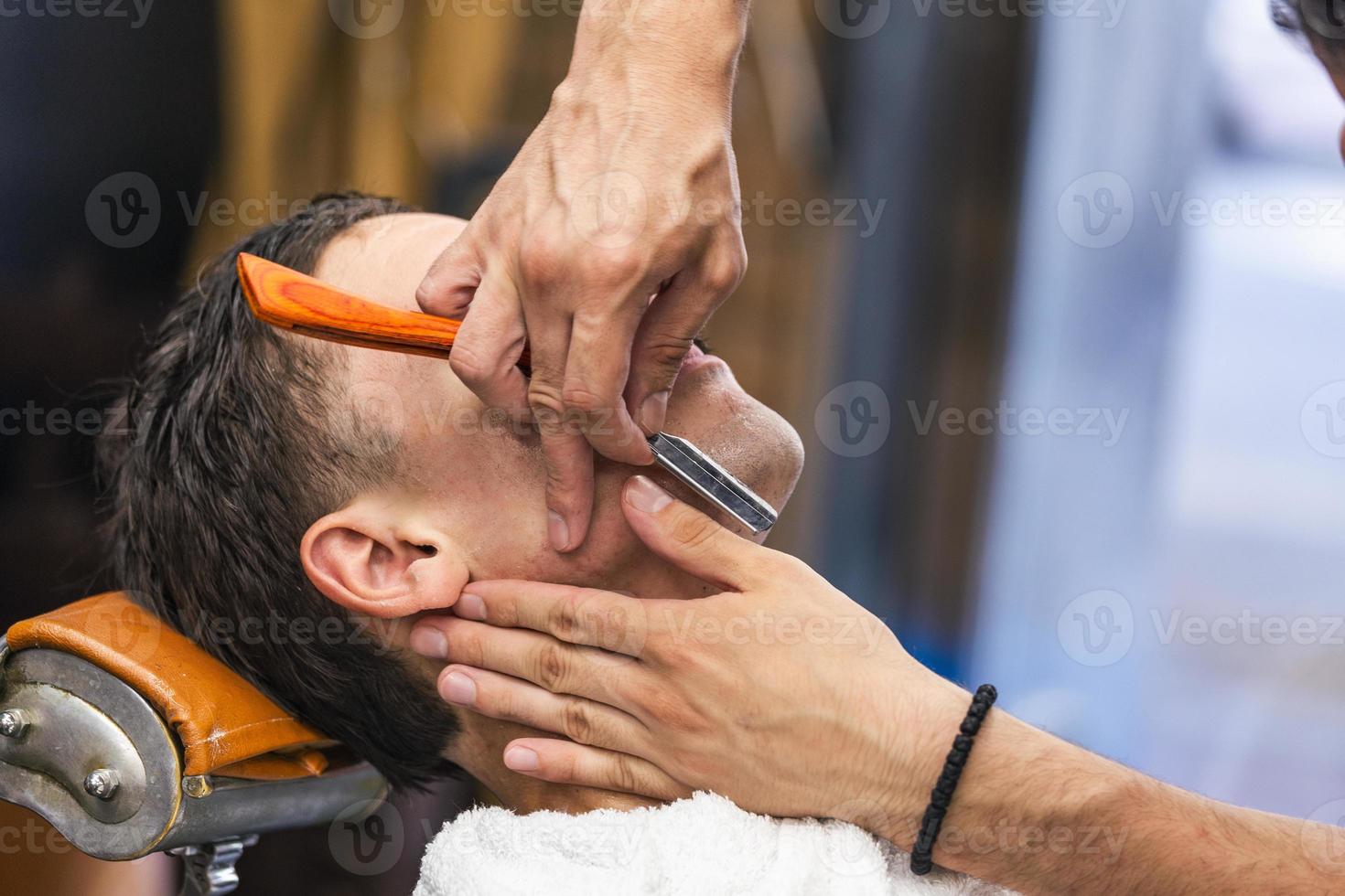 rasoir dans les mains d'un coiffeur spécialisé. coiffeur rasant un homme dans un salon de coiffure, gros plan. homme mith moustaches ayant un rasage photo