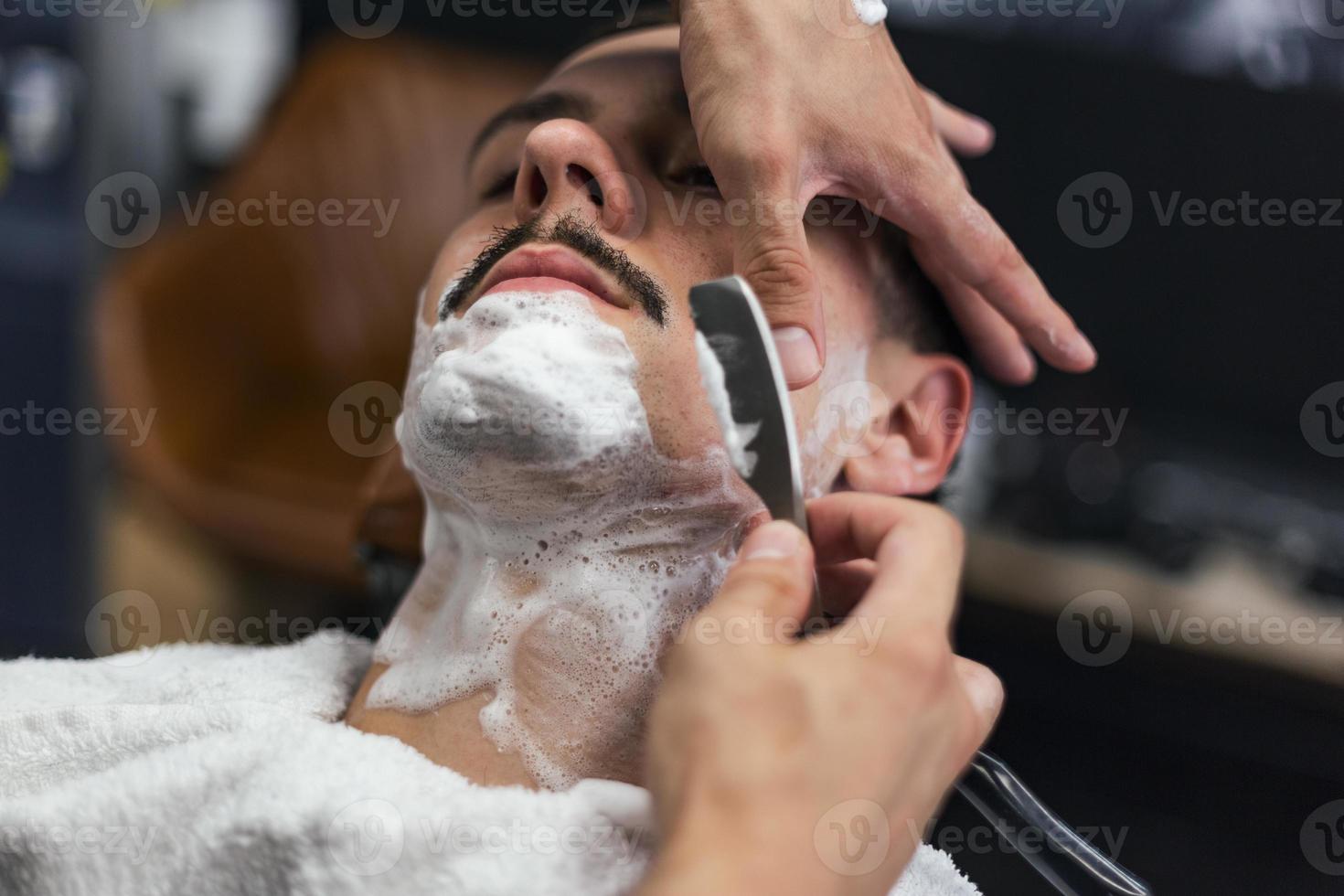 homme mith moustaches ayant un rasage. rasoir dans les mains d'un coiffeur spécialisé. jeune homme se rase à l'ancienne au salon de coiffure. gros plan, imagerie de style rétro photo