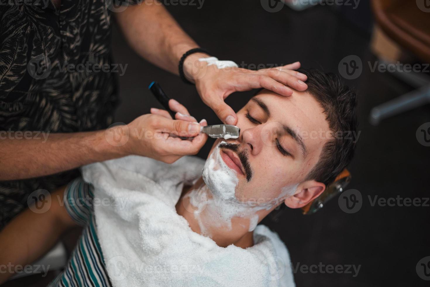 homme mith moustaches ayant un rasage. rasoir dans les mains d'un coiffeur spécialisé. jeune homme se rase à l'ancienne au salon de coiffure. gros plan, imagerie de style rétro photo